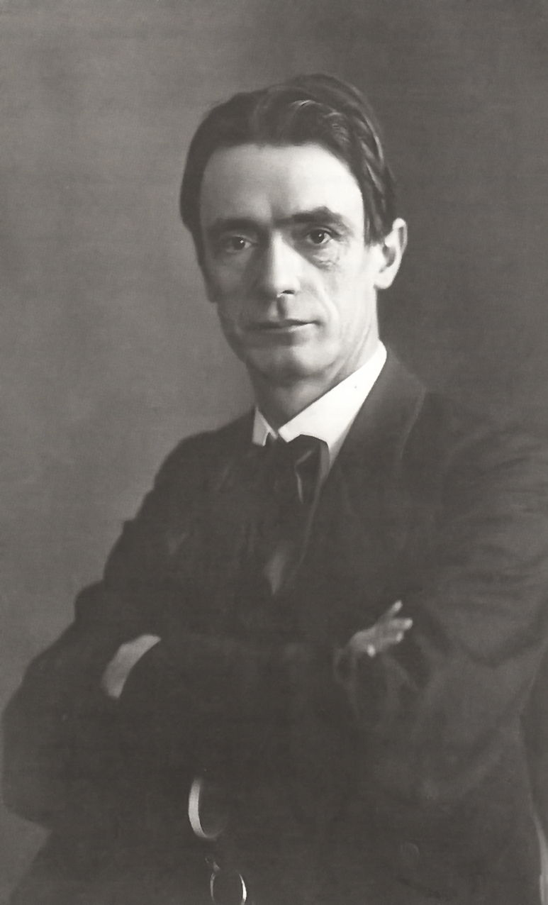 Formal photographic portrait of Rudolf Steiner around 1905, seated in a dark coat, hair swept back, gazing directly at the viewer.