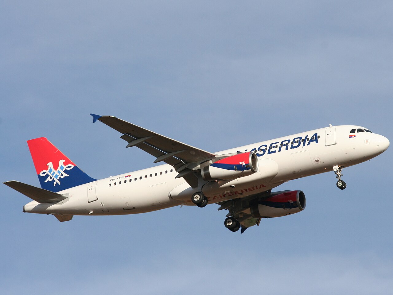 A white Air Serbia Airbus A320 airliner, landing gear down, on final approach against a pale blue sky; tail registration reads YU-APG.