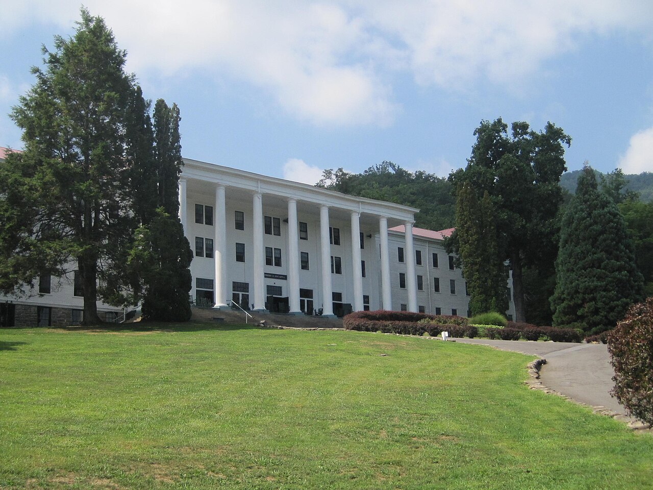 A large white neoclassical building with a tall columned portico set against wooded Blue Ridge hills — Robert E. Lee Hall, the college's first home.