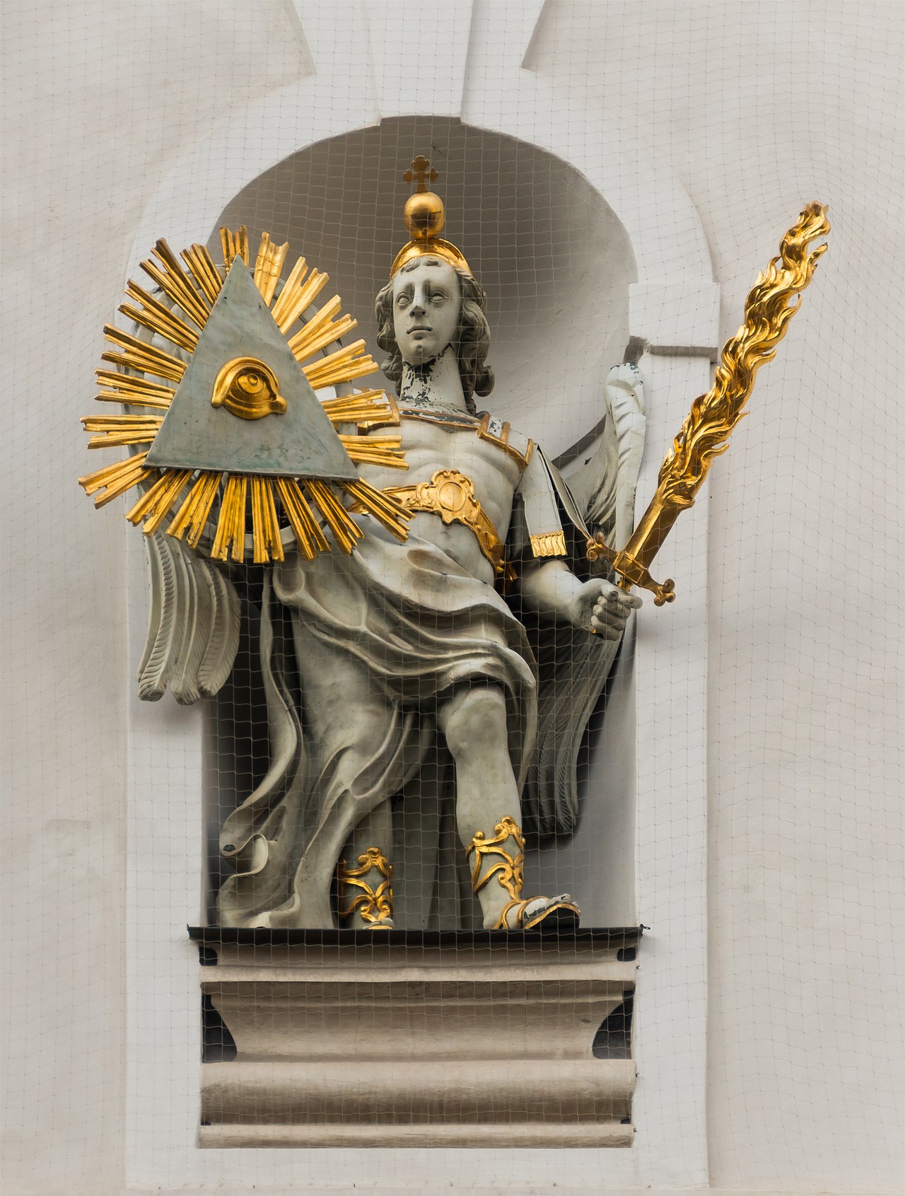Weathered stone statue of Saint Michael the archangel on the facade of a church, sword raised.