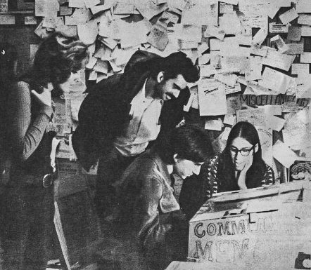 A Teletype ASR-33 terminal inside a cardboard enclosure standing on the floor of Leopold's Records in Berkeley, 1973, with people gathered around it.