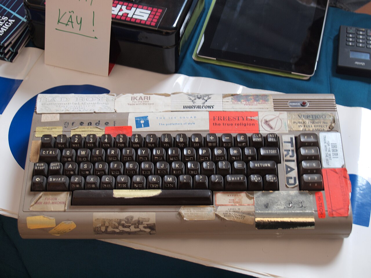 A Commodore 64 keyboard plastered edge to edge with cracking- and demo-group stickers and handles.
