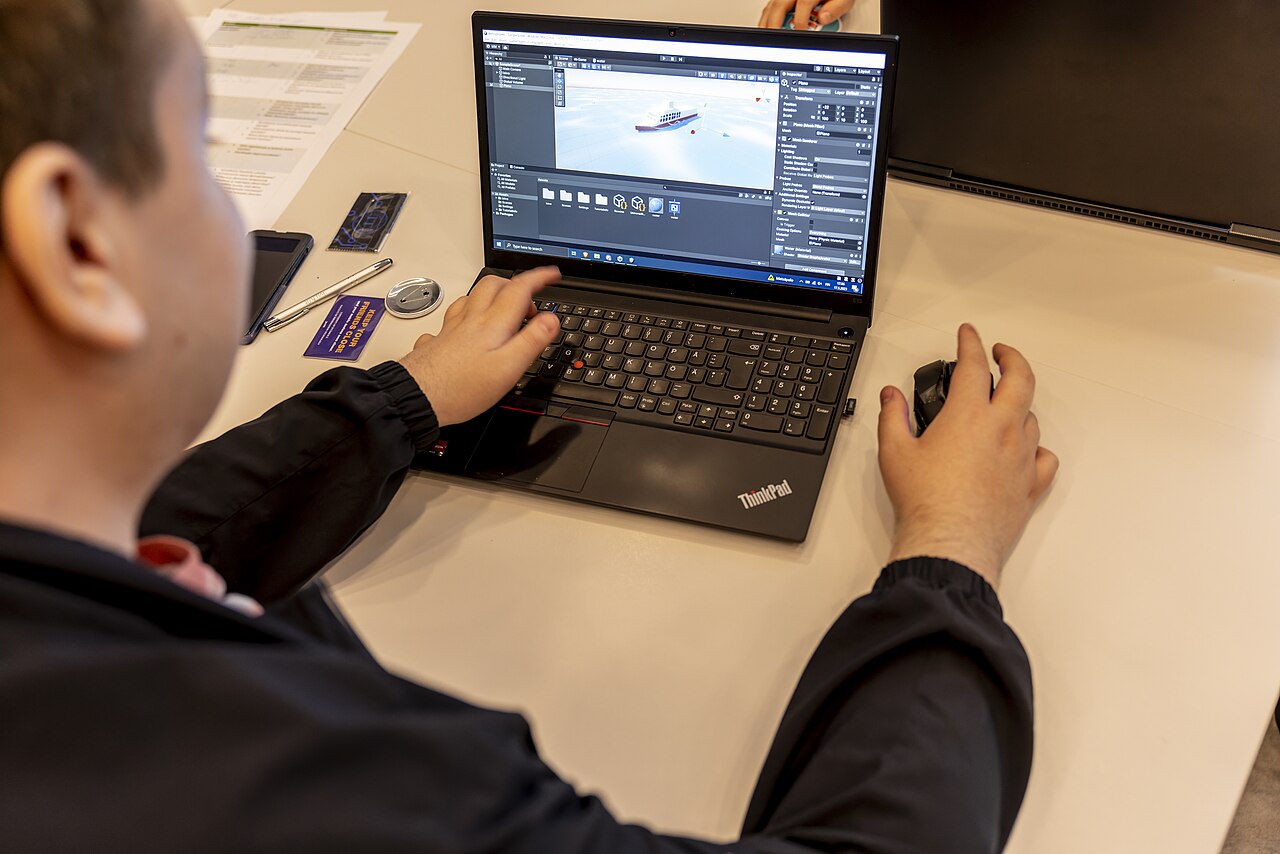 A person at a laptop running a 3D game/real-time engine at a museum demoscene workshop.