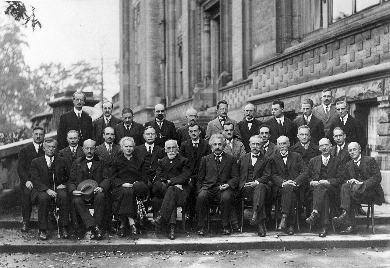 The 1927 Solvay Conference on Quantum Mechanics: rows of physicists including Einstein, Curie, Bohr, and Planck seated and standing for a formal group portrait — the archetypal gathering of elite scientific minds in one room.