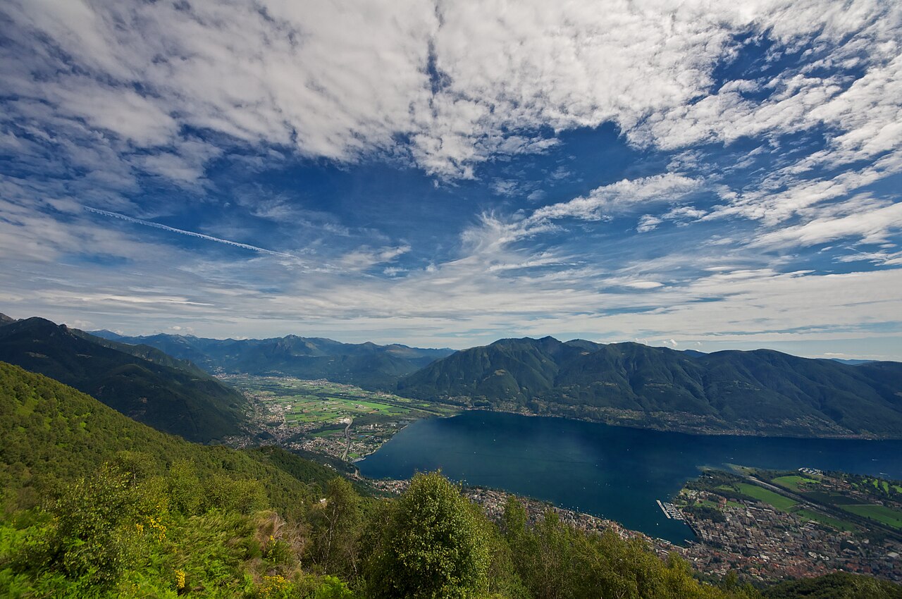 Aerial view south over Lake Maggiore in Ticino, Switzerland, with the Ascona and Locarno peninsula on the shore and mountains rising on both sides of the lake.