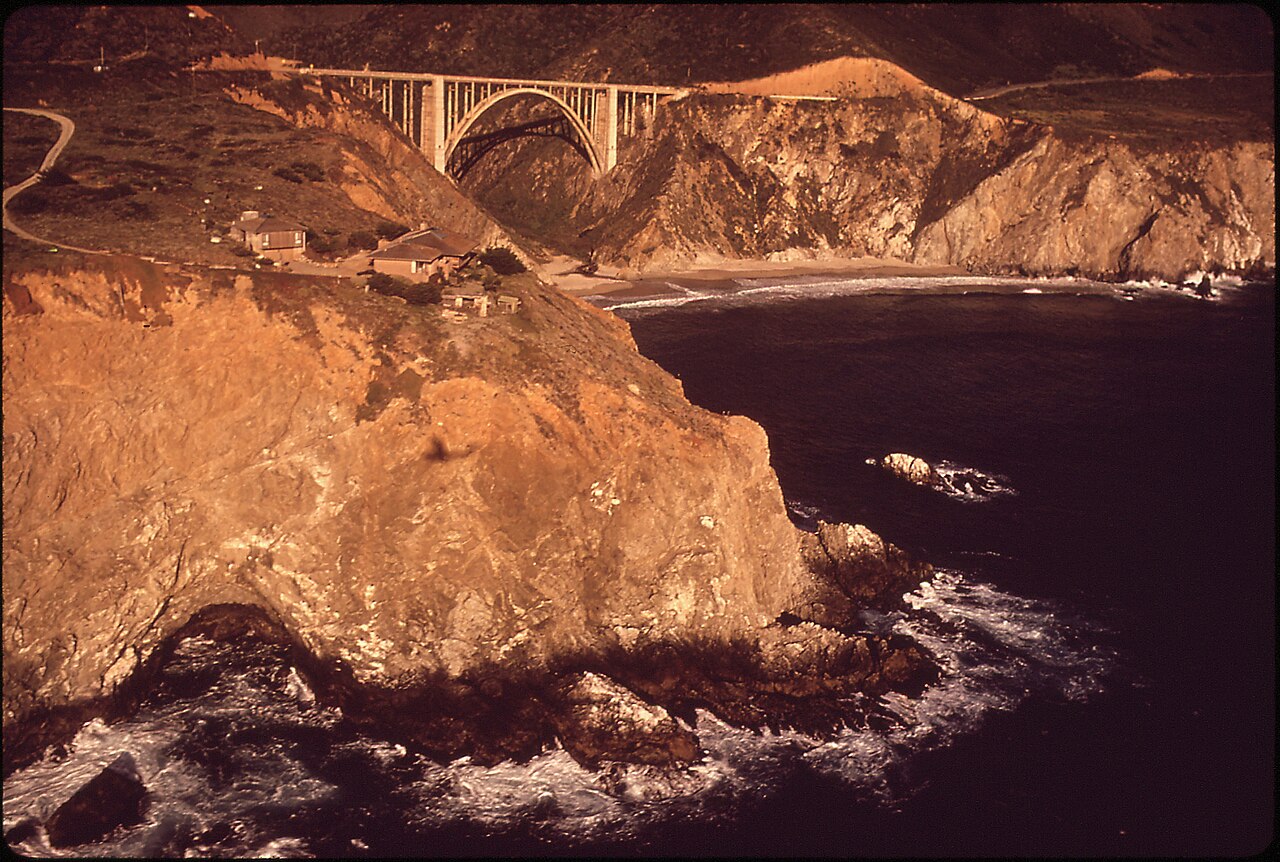 A natural sea cave and rock bridge on the California coast, waves washing through the arch.