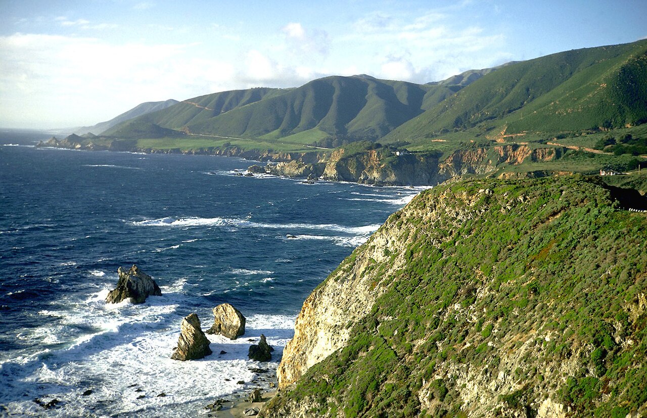 The Pacific coastline of Big Sur, California, in spring 1969 — cliffs meeting the sea beneath a hazy sky.