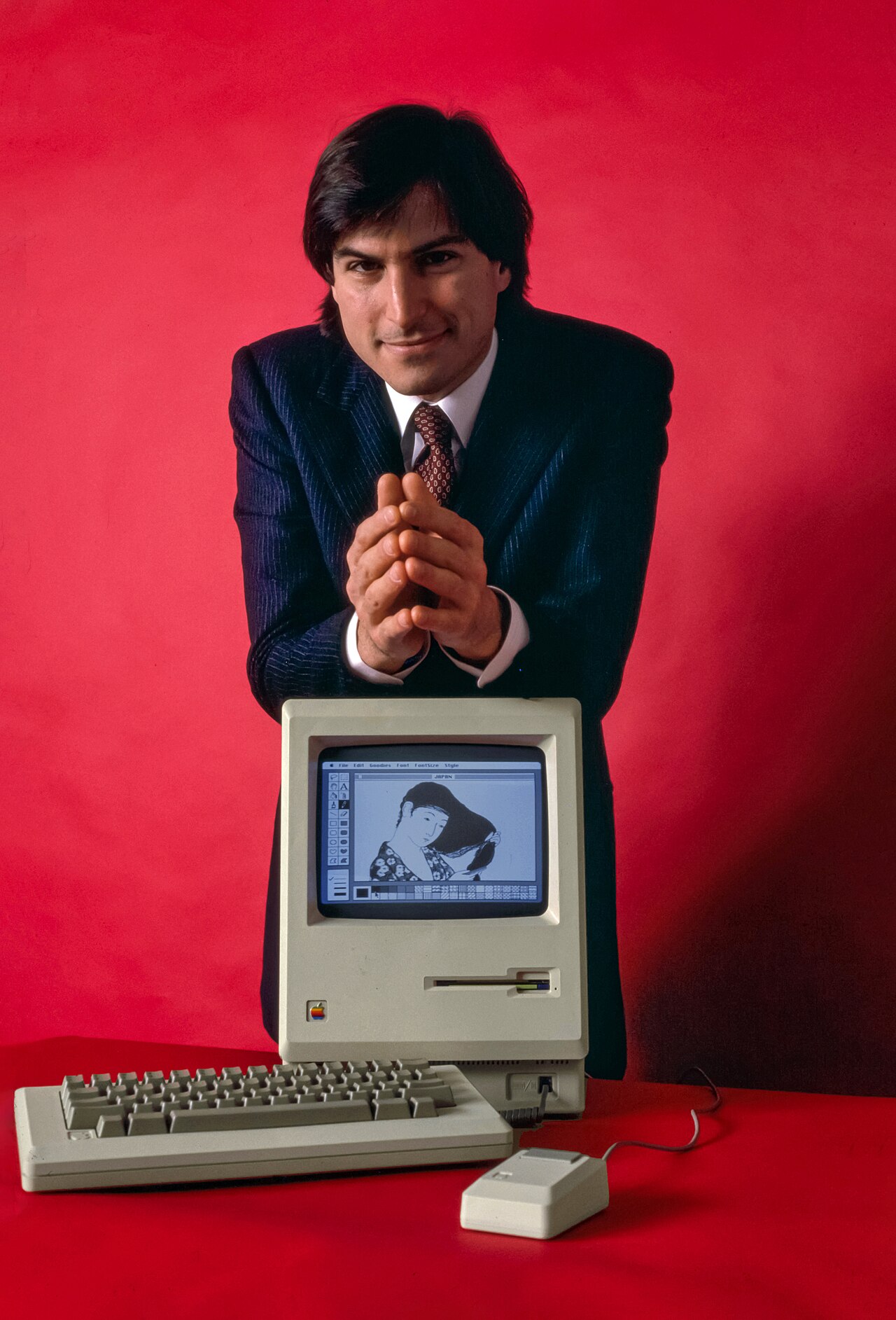 Steve Jobs seated beside an early Macintosh computer in January 1984.