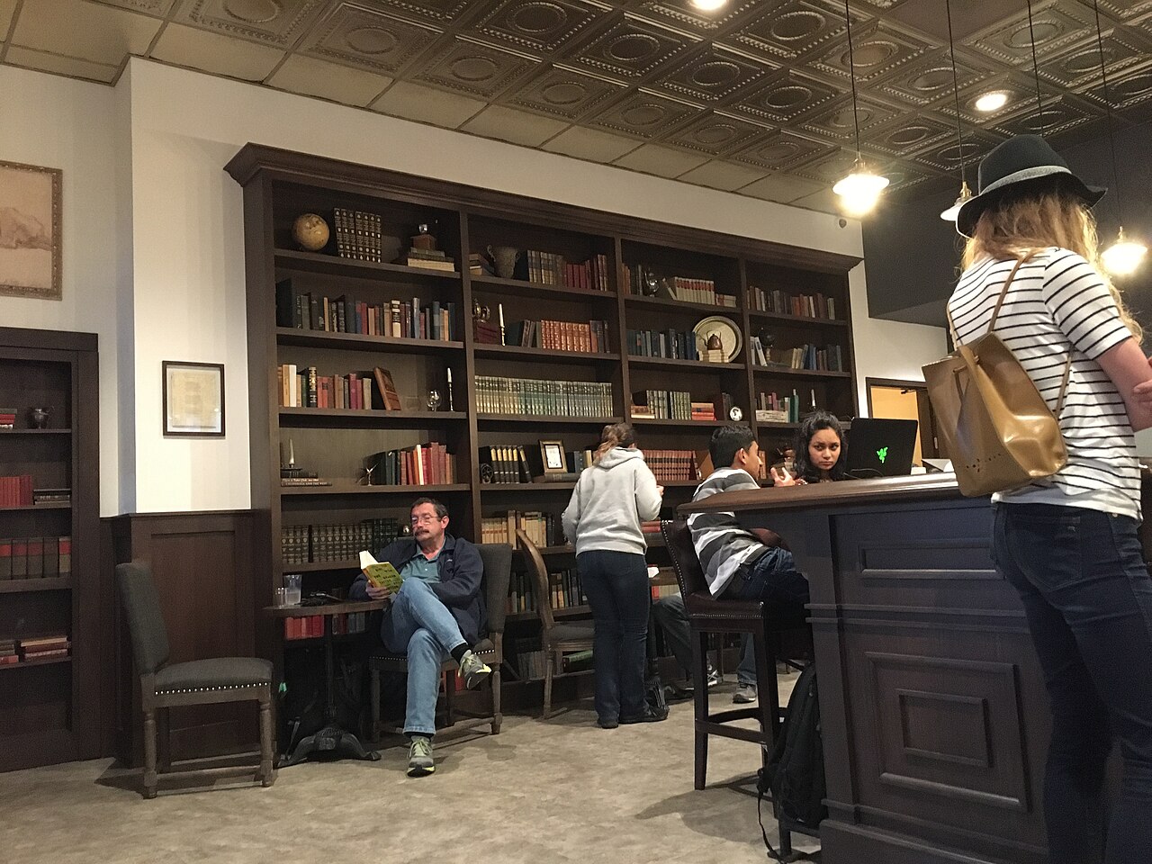 A book-lined, dark-oak room with a tall bookcase and a man reading in an armchair, in a present-day café named Inklings.