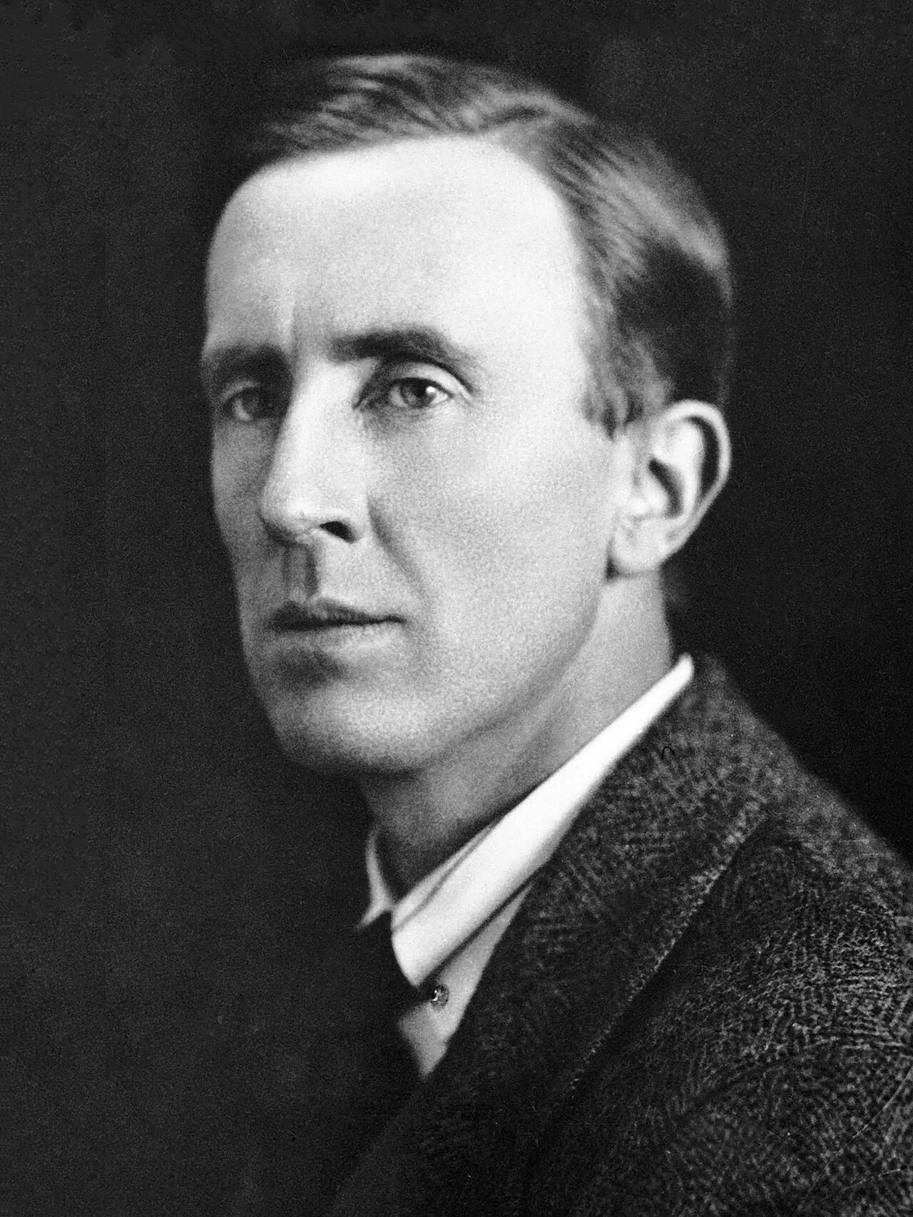 Black-and-white studio portrait of a young J.R.R. Tolkien, mid-1920s, in a tweed jacket against a dark ground.
