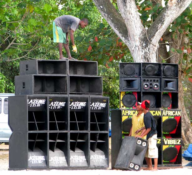 Preparations for a sound-system performance, with equipment and speaker stacks being assembled.