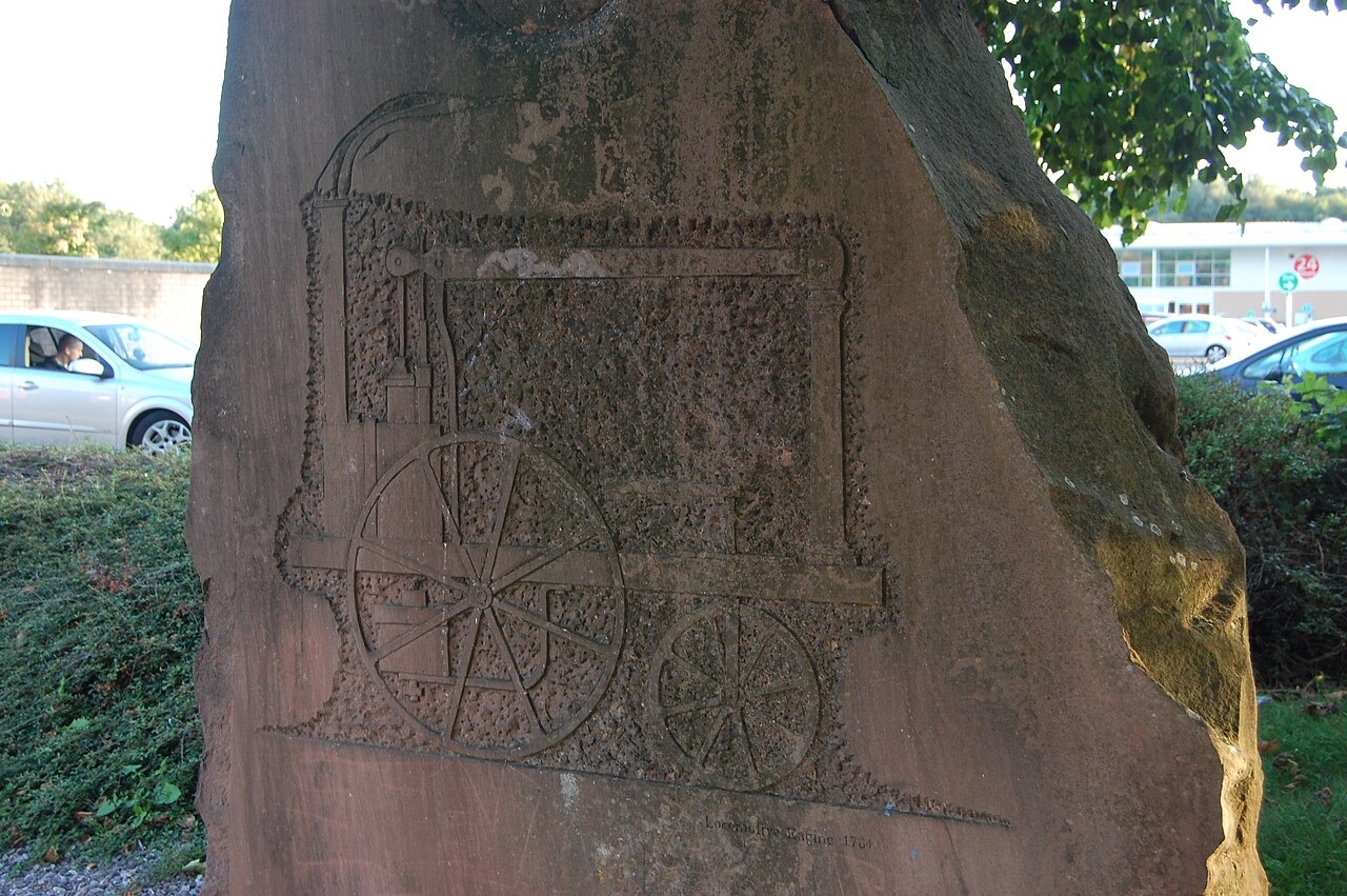 Close detail of the carved locomotive engine — boiler, spoked wheels, and chimney — cut in low relief into weathered red sandstone.