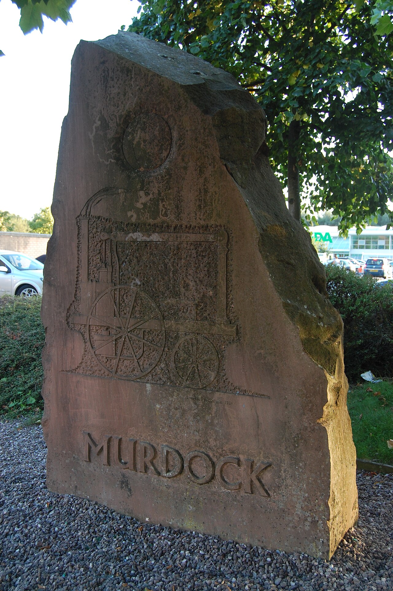 A red-sandstone monolith with a carved full-moon disc above a low-relief locomotive engine and the incised name MURDOCK.