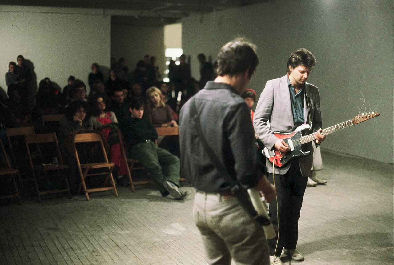 Black-and-white photograph of composer Glenn Branca performing on stage, guitar in hand, at Hallwalls in the 1980s.