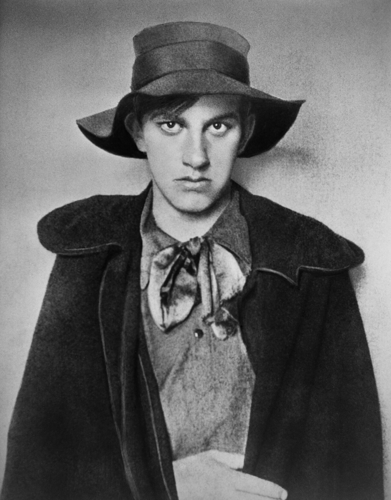 Studio portrait of the young Vladimir Mayakovsky in a wide-brimmed hat and cape, glowering at the camera, circa 1910.