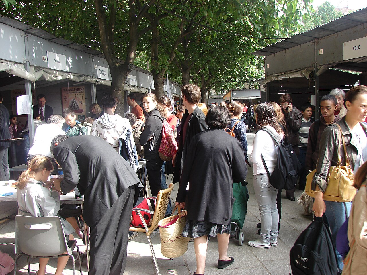 A crowded outdoor avenue of booths at a modern Paris culture-and-mathematics fair, with visitors browsing stalls beneath trees.