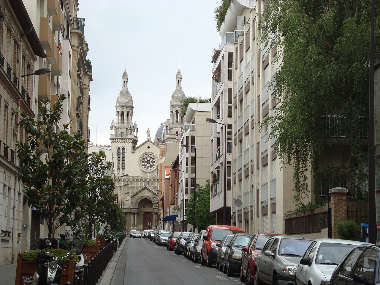 View down Rue Charles-Fourier in the 13th arrondissement of Paris — a quiet street of apartment blocks and parked cars closing on a domed church.