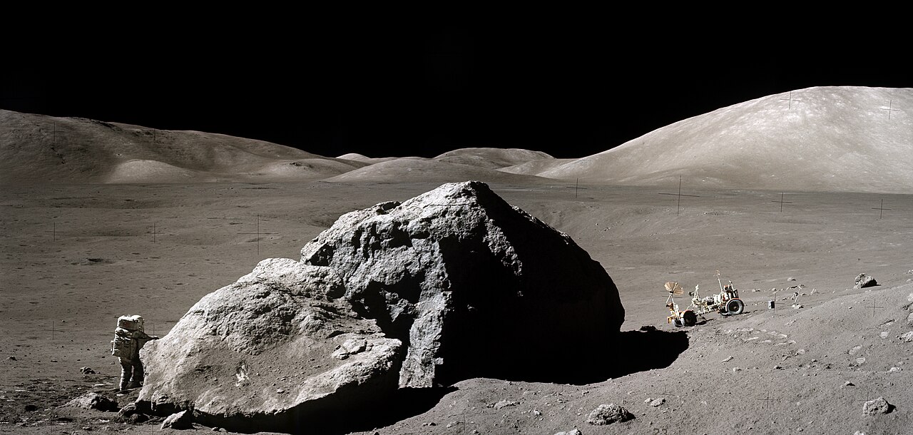 Apollo 17 lunar surface photograph: a large split boulder known as Tracy's Rock in the foreground with the grey Taurus-Littrow valley and the black sky of the Moon beyond.